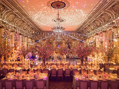 Elegant banquet hall with ornate chandeliers, intricate ceiling designs, and lavishly decorated dining tables adorned with flowers and candles, set for a formal event.